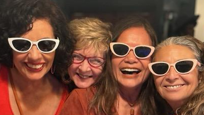Four friends laughing together in matching white sunglasses at a Girls’ Night Out celebration.